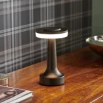 Dark metal version of the cordless table lamp with lit ring light, standing on a desk
